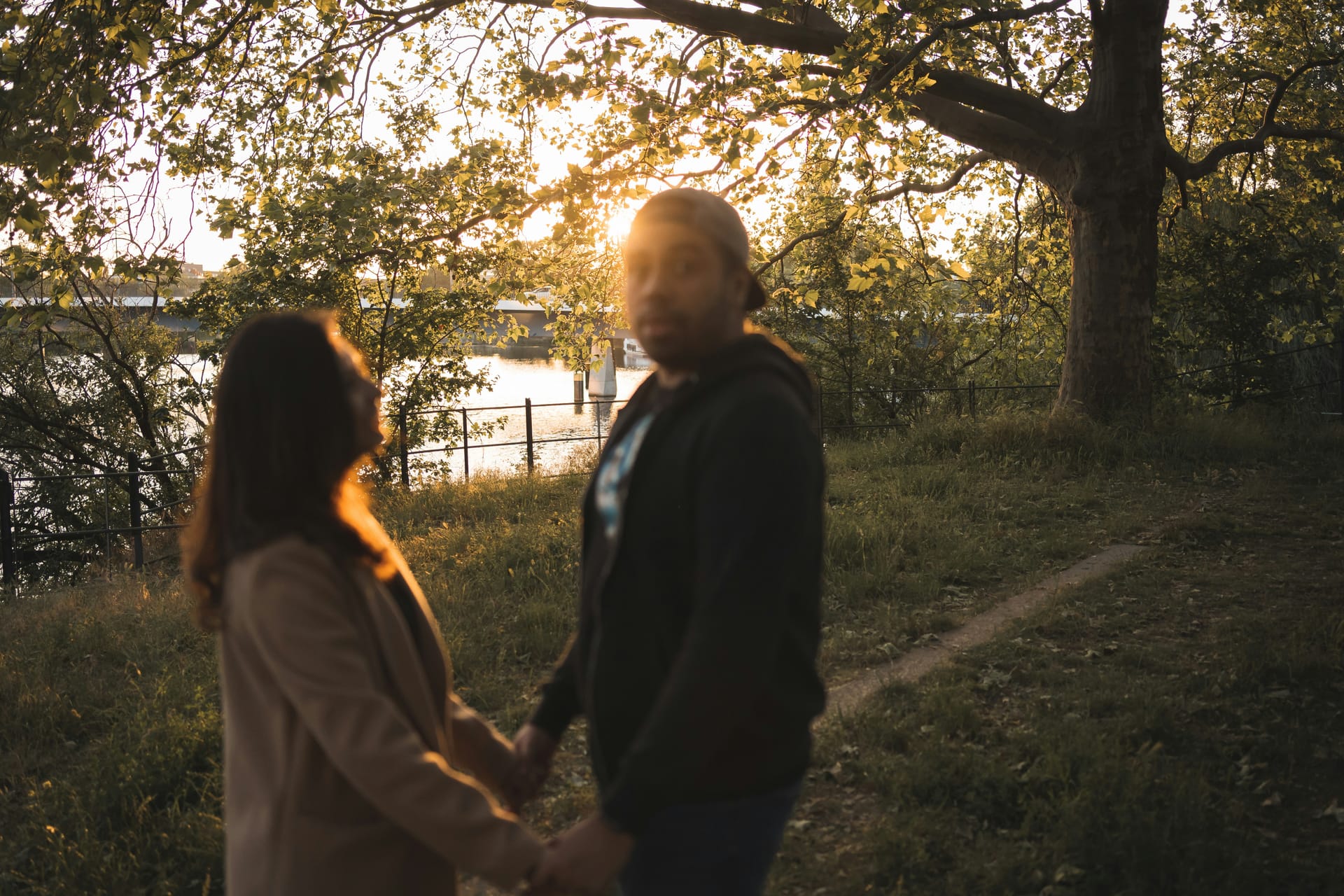 Young couple holding hands walking together in sunset park setting